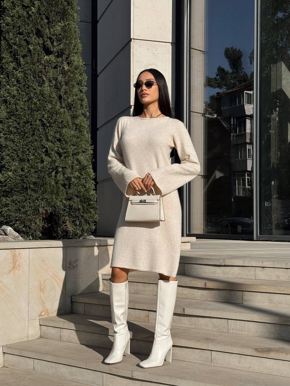 Woman in a white outfit with knee-high boots standing on steps outdoors.