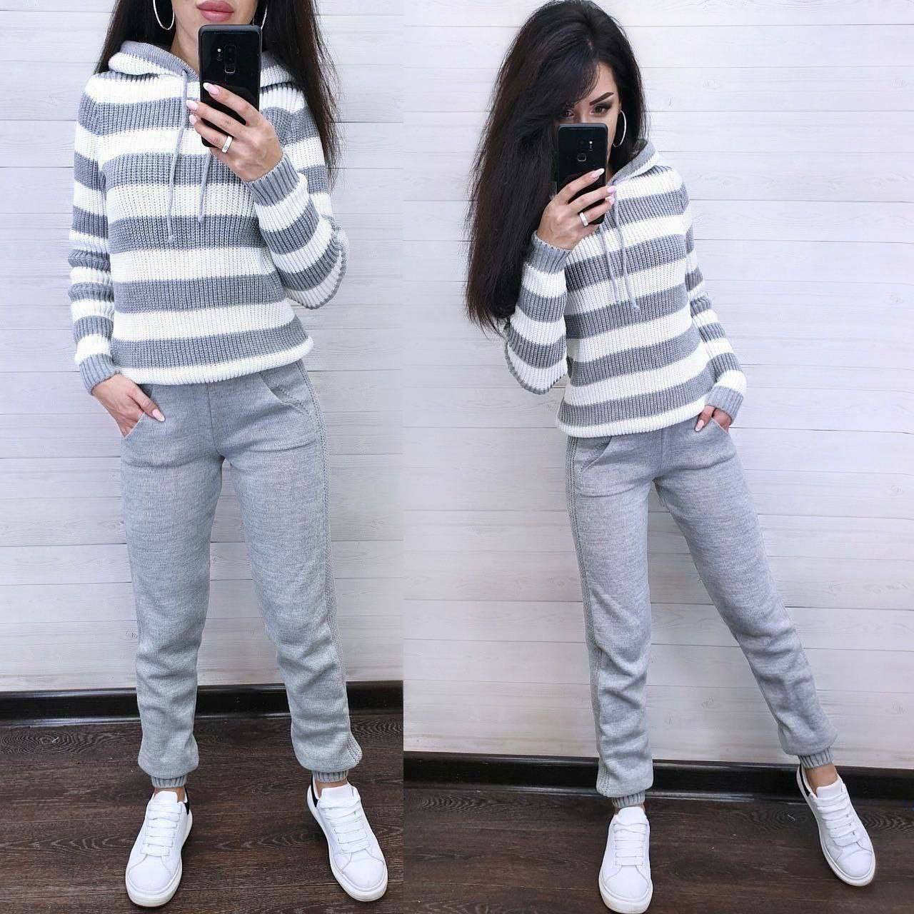 Person wearing a gray and white striped sweater and gray sweatpants, standing against a white wall.