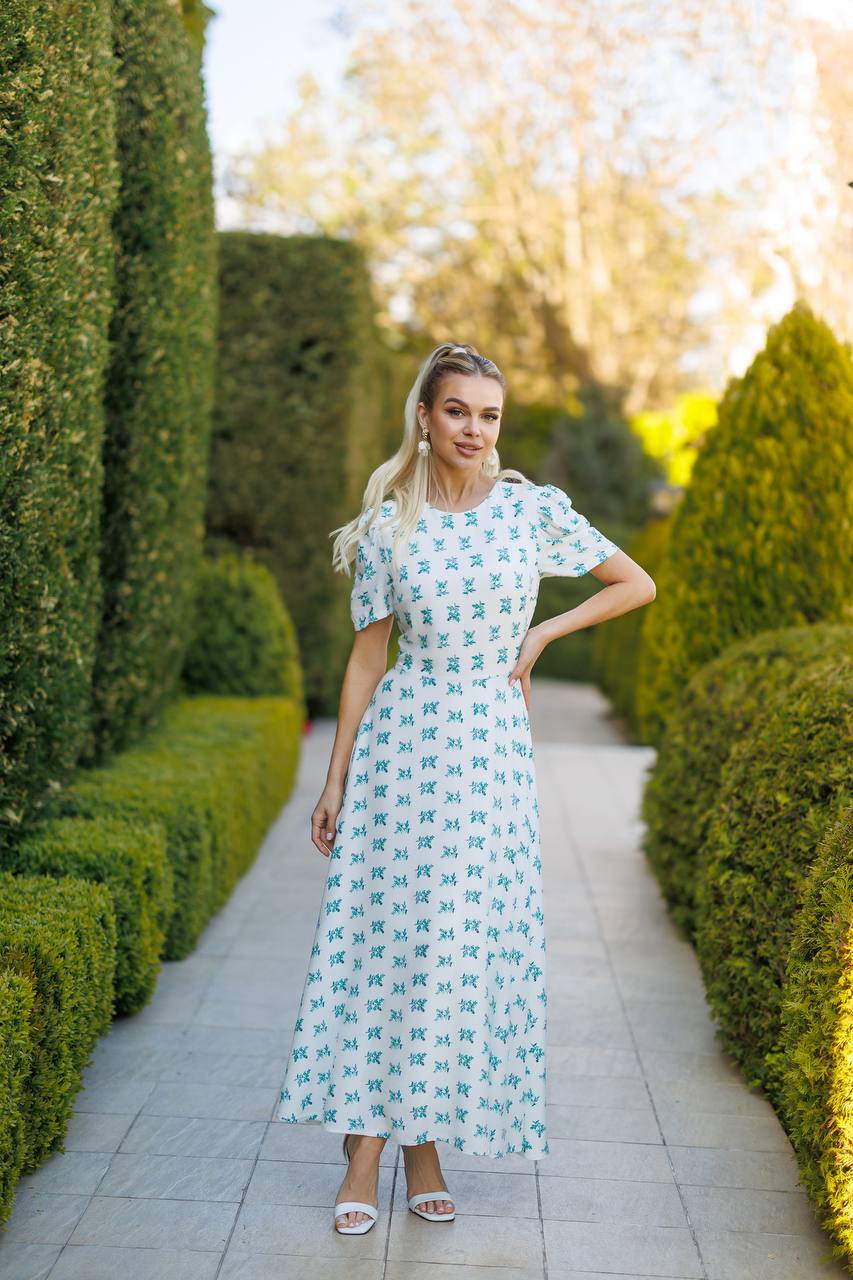 Woman in a floral dress standing in a garden with manicured hedges.