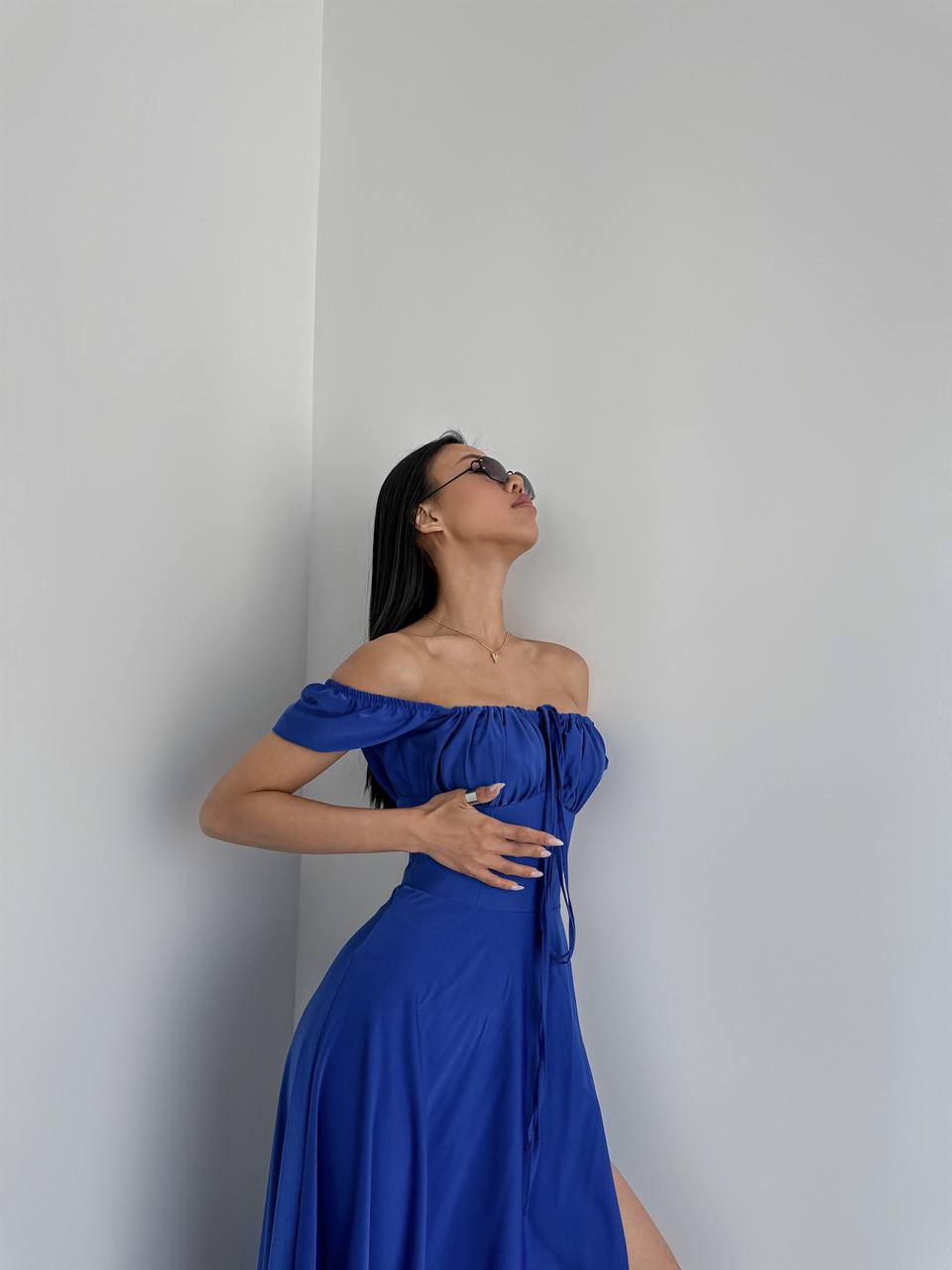 Woman in a blue off-shoulder dress against a plain white wall