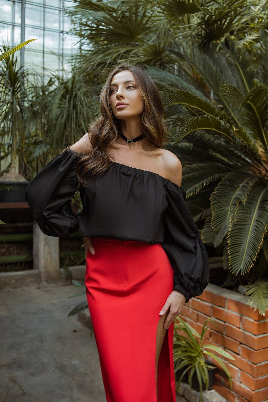 Woman in black top and red skirt standing in a greenhouse with plants.