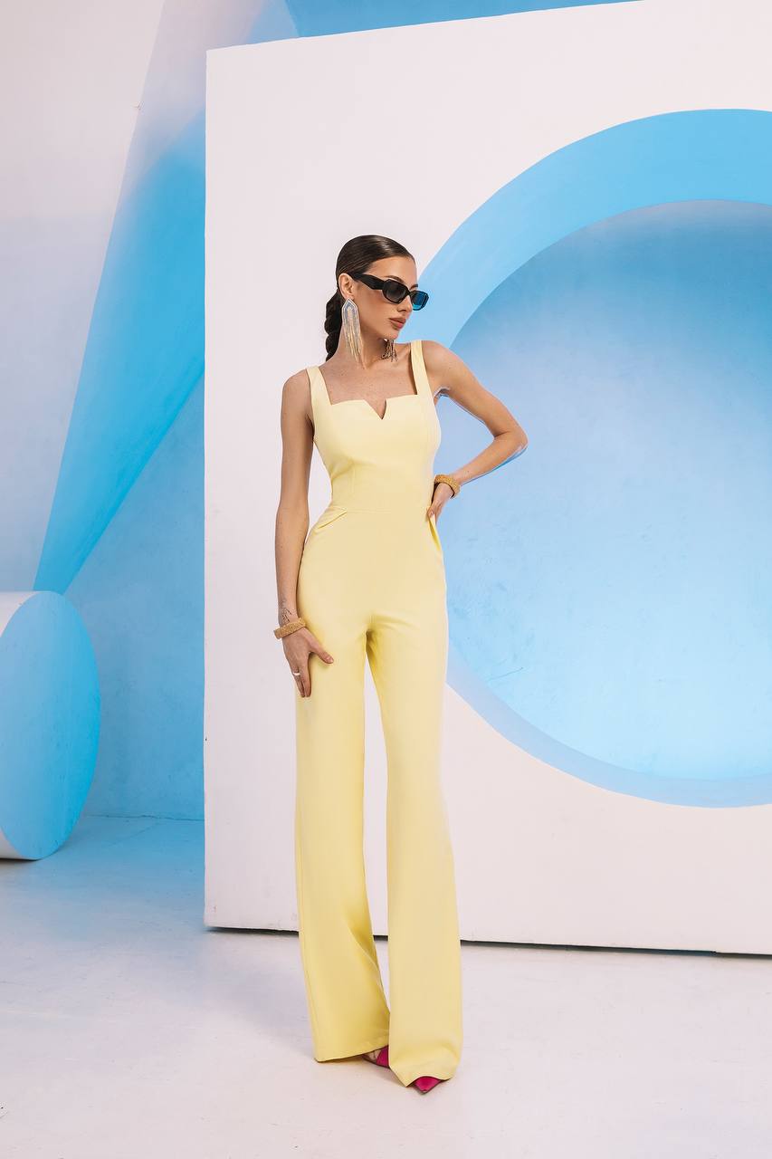 Woman in a yellow jumpsuit posing against a blue and white abstract background