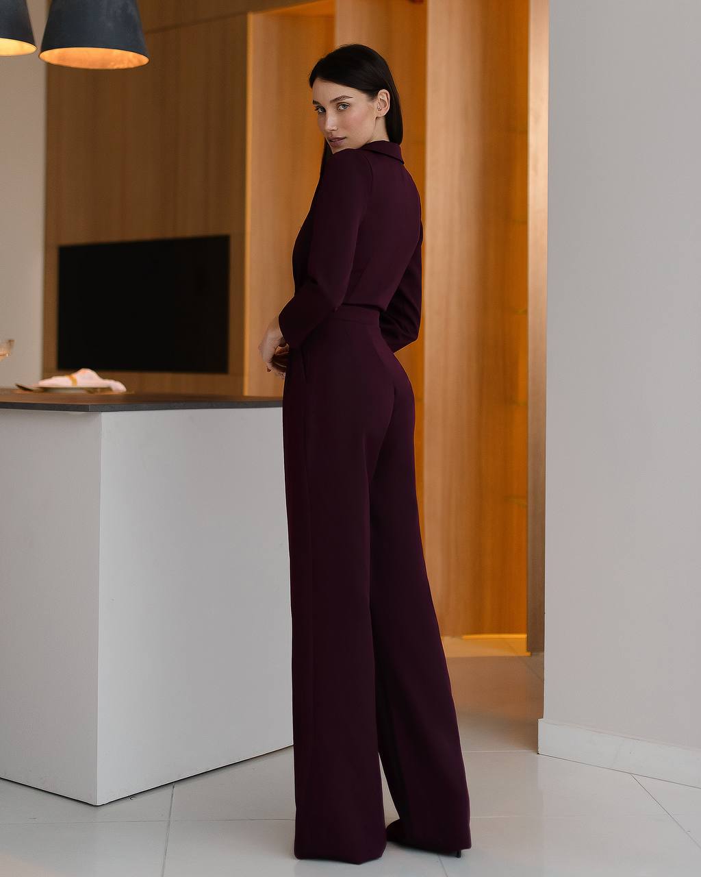 Woman in a burgundy jumpsuit standing in a modern interior setting.