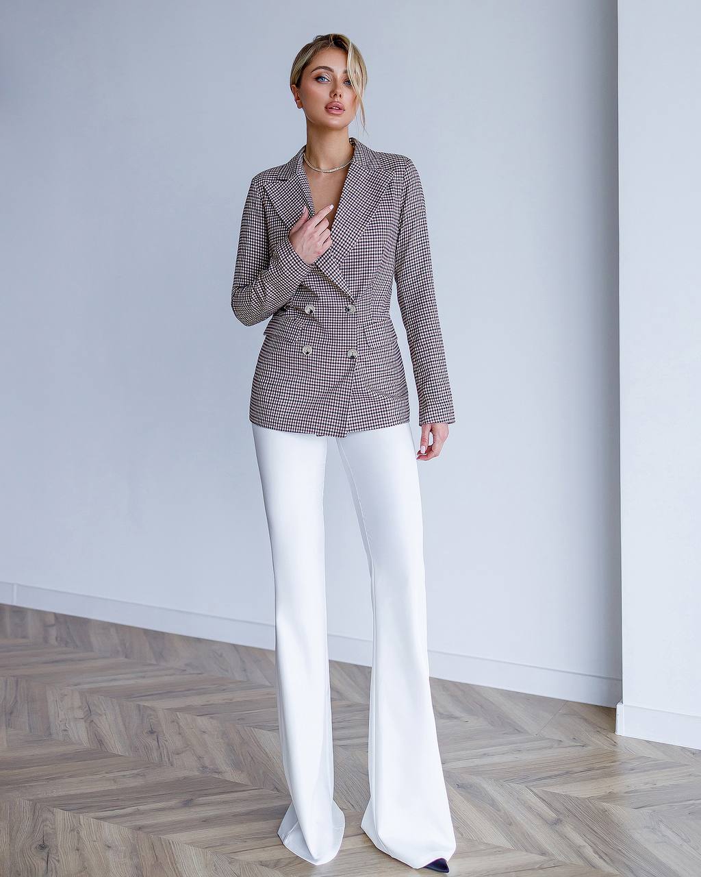 Woman wearing a checkered blazer and white pants in a minimalistic setting