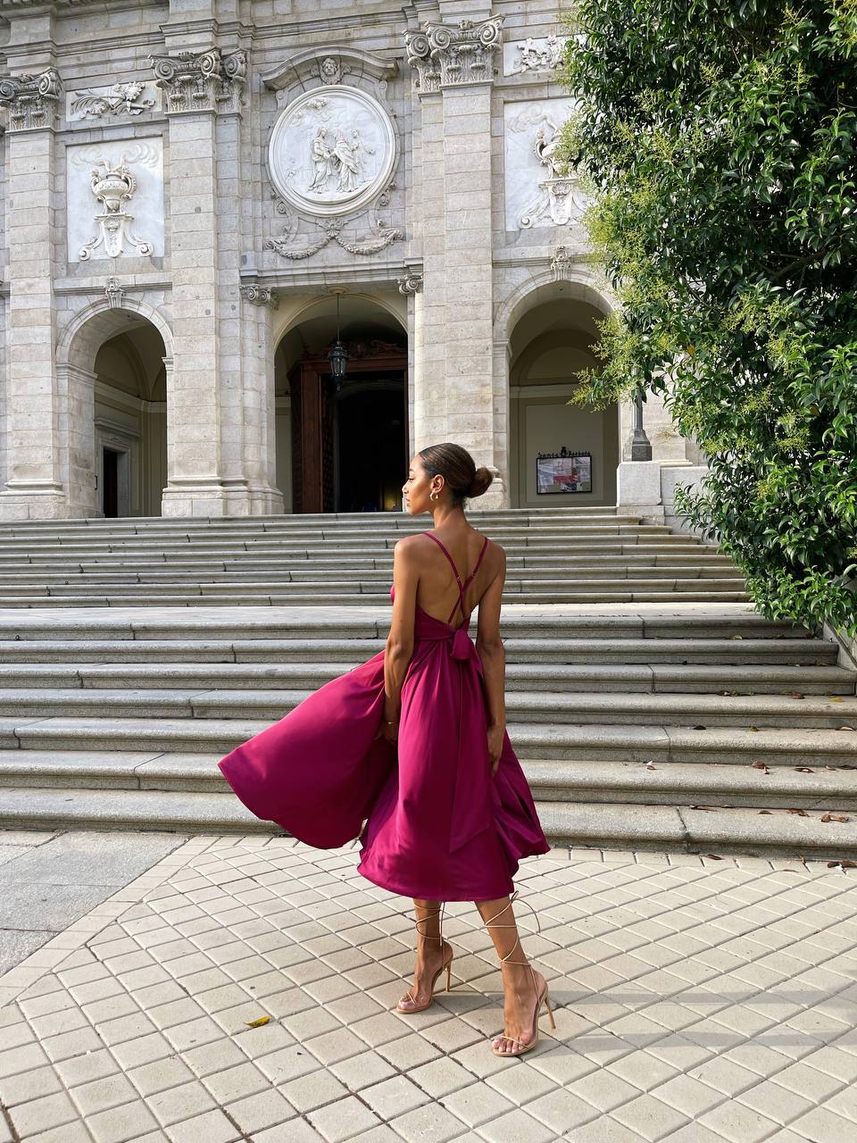 Woman in a pink dress standing in front of an ornate building with steps.