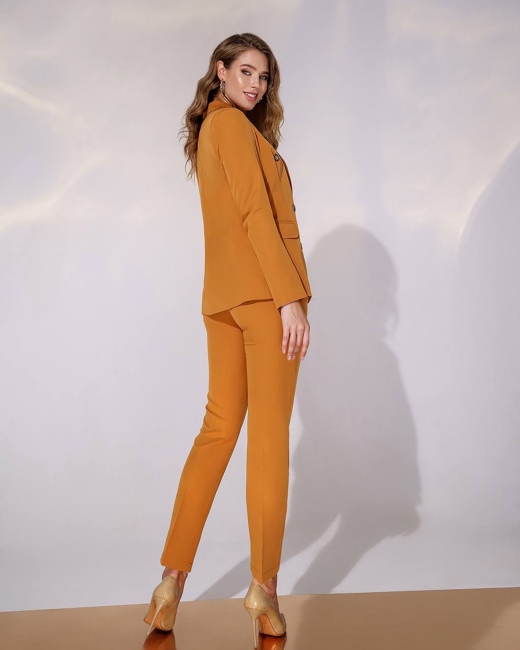 Woman wearing a mustard yellow suit against a white background