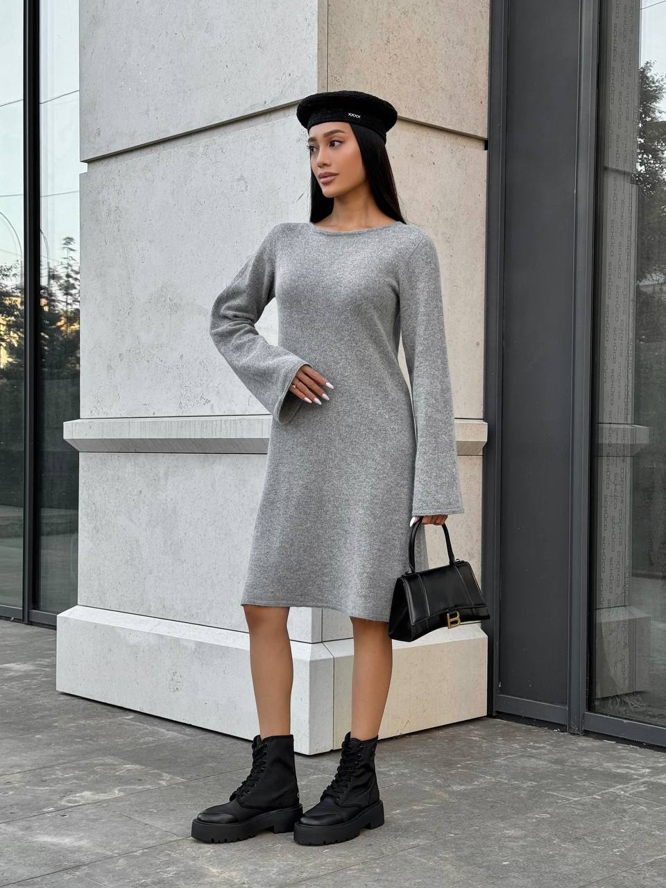 Woman in a gray dress and black boots standing outside a building.