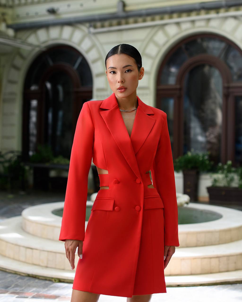 Woman wearing a red suit standing in front of an architectural building.