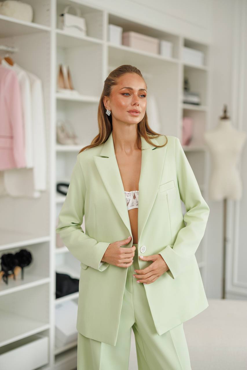 Woman wearing a light green suit in a room with shelves and mannequins.