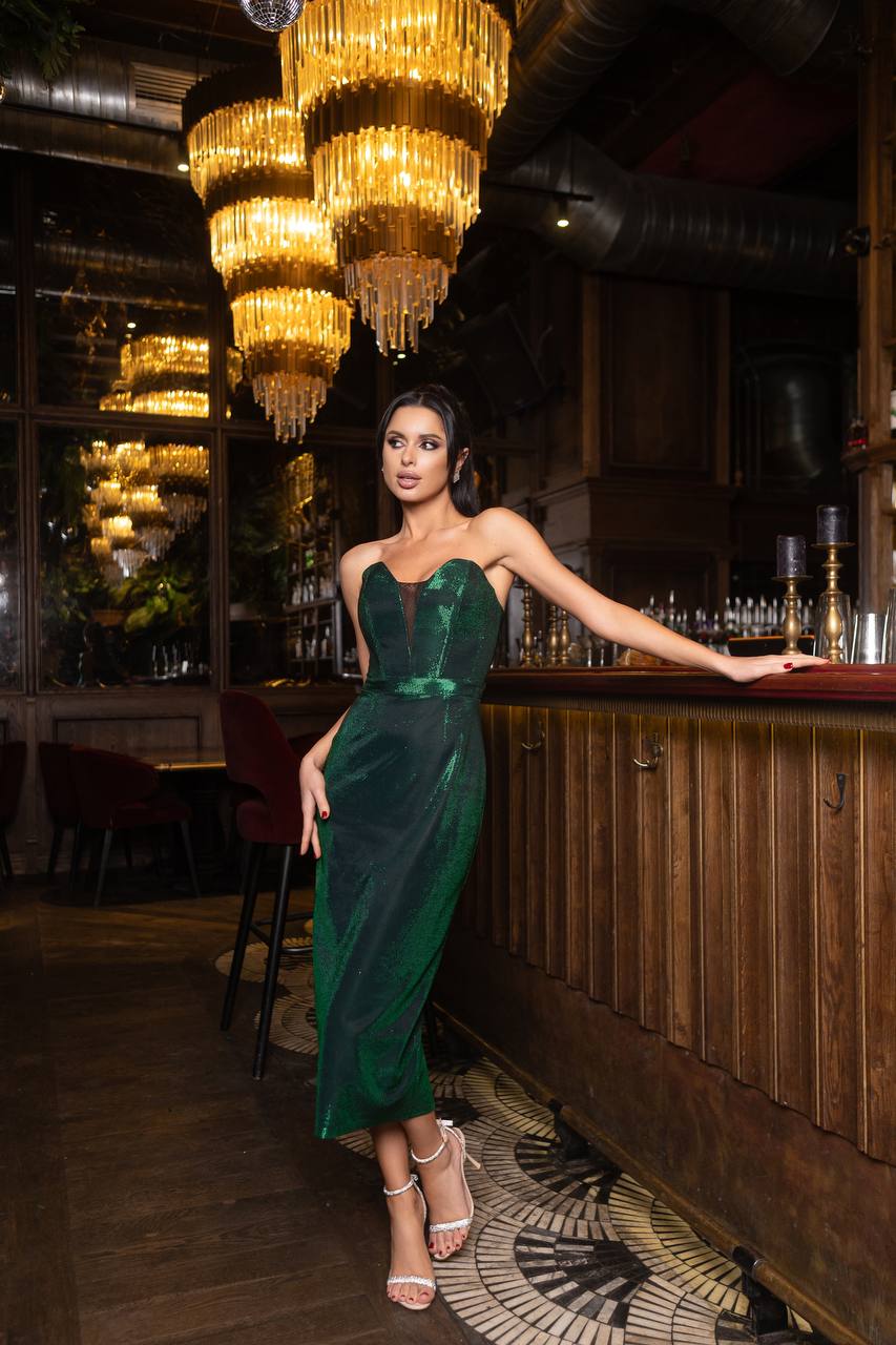 Woman in a green dress standing in a bar with chandeliers hanging above.