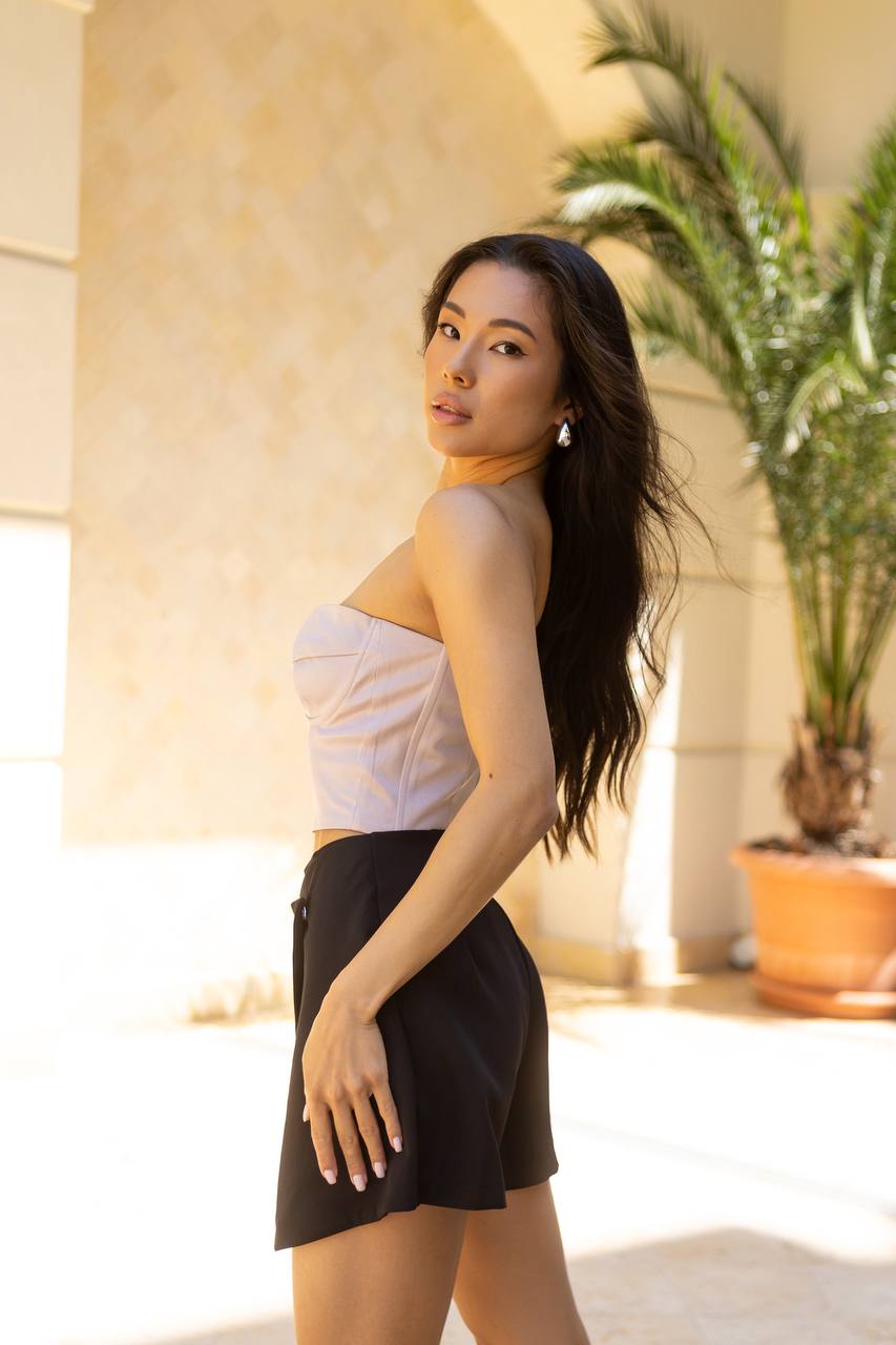 Woman in a white top and black skirt standing outdoors with plants in the background