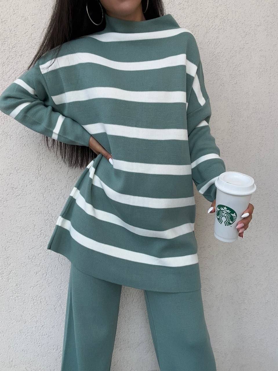 Person wearing a green and white striped outfit holding a Starbucks cup against a plain background