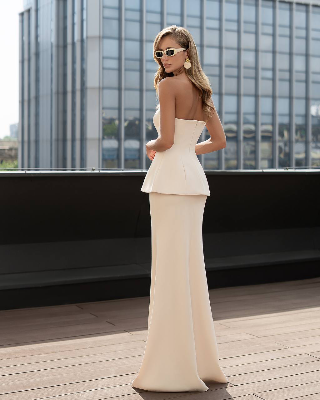 Woman in a white peplum dress standing on a rooftop with cityscape background