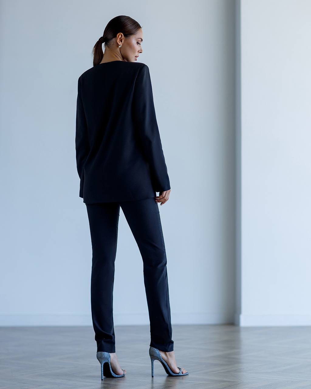 Woman wearing a black suit standing against a plain white wall.