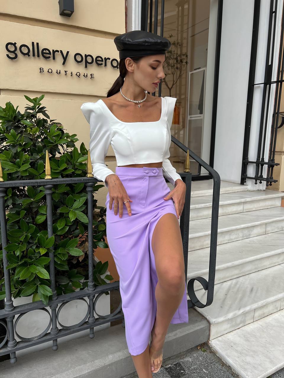 Woman in a white top and purple skirt standing in front of 'Gallery Opera Boutique'.