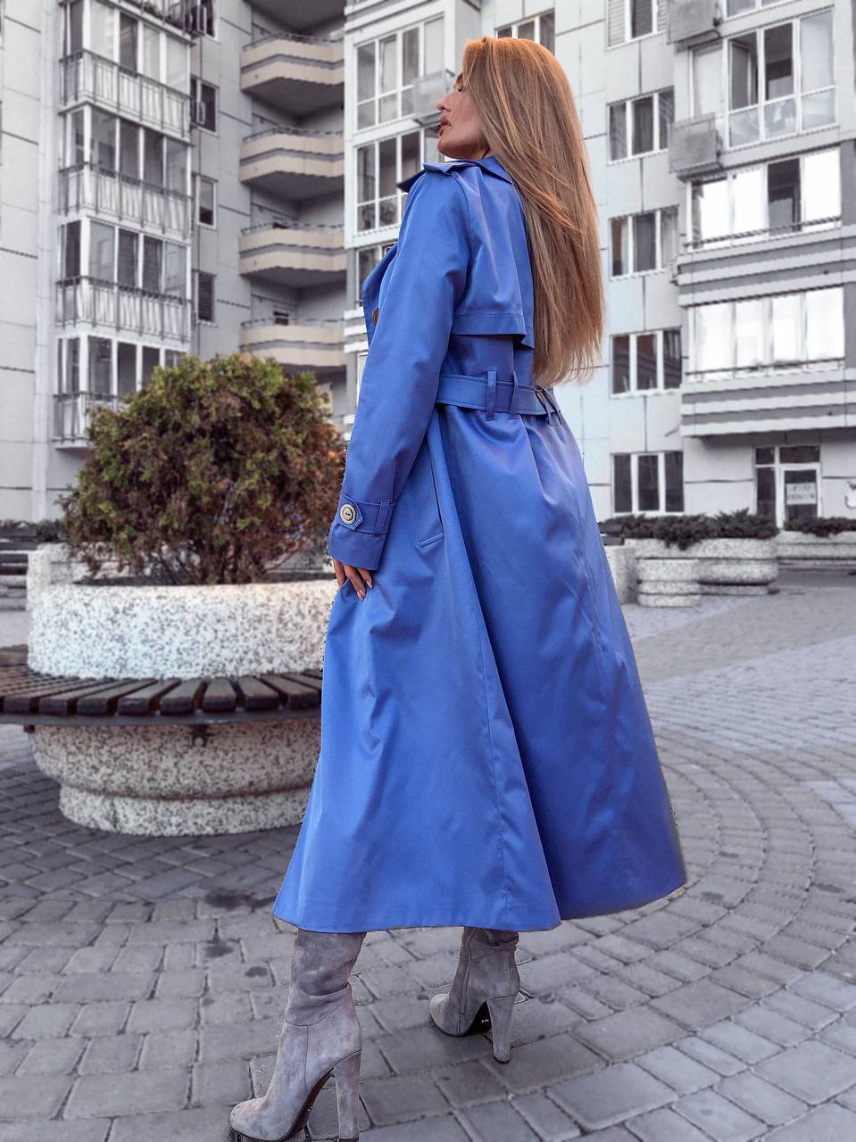Woman wearing a blue trench coat standing on a city street.