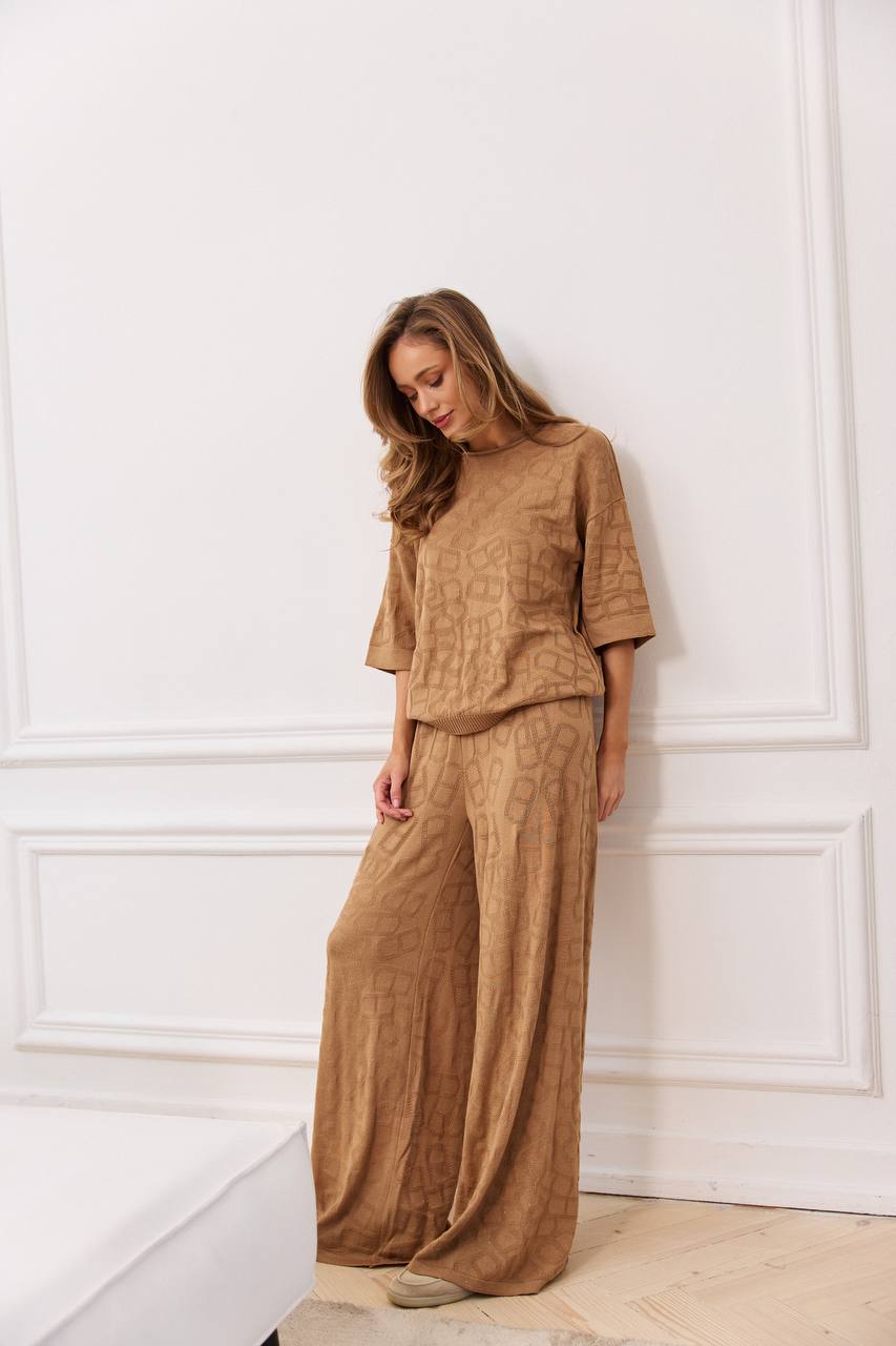 Woman wearing a brown outfit standing against a white paneled wall.