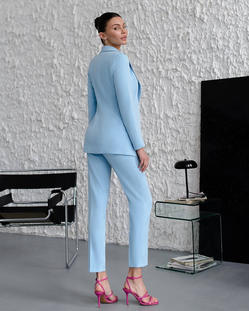 Woman in a light blue suit standing in a modern room with a textured white wall.