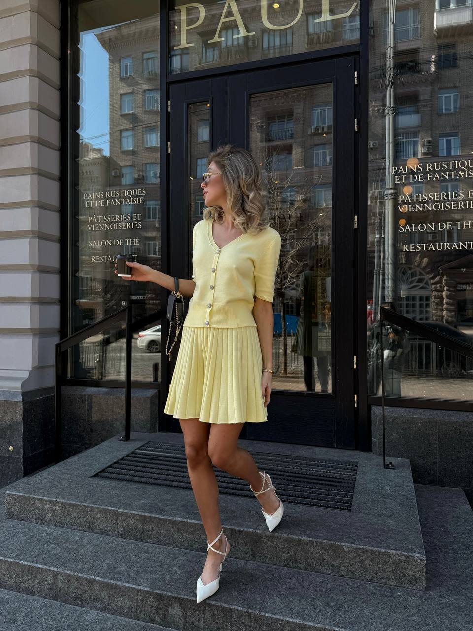 Woman in a yellow dress standing on steps outside a building with large glass doors.