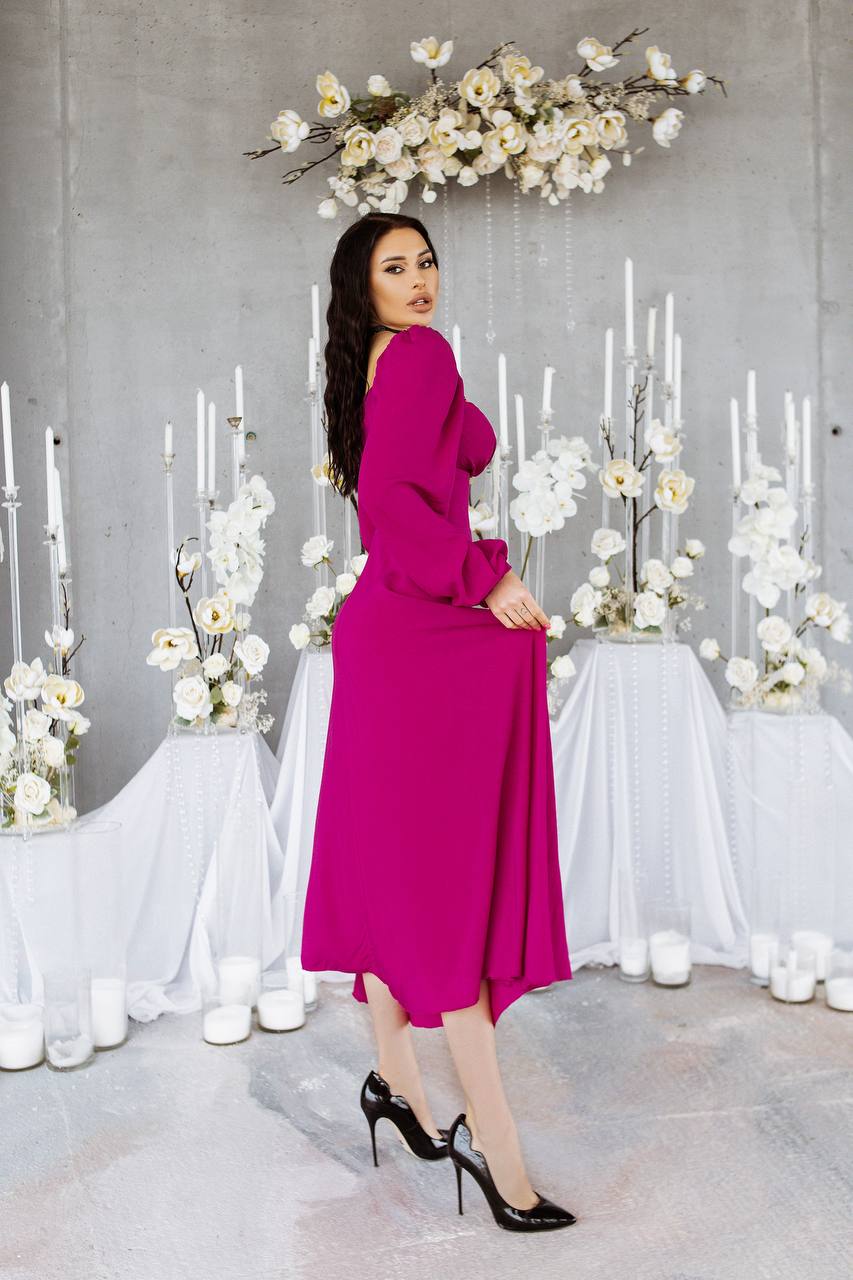 Woman in a pink dress standing in front of decorative floral arrangements and candles.