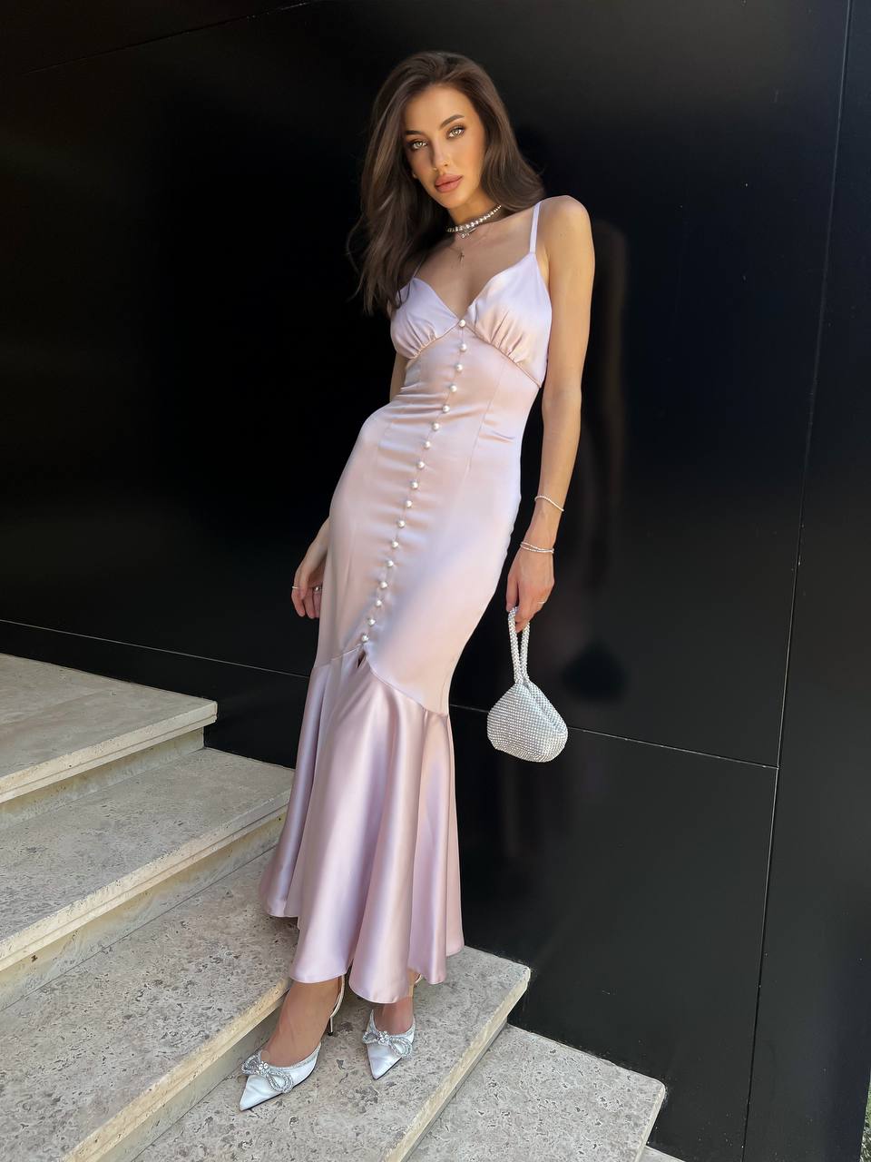 Woman in a light pink dress standing on steps against a black wall