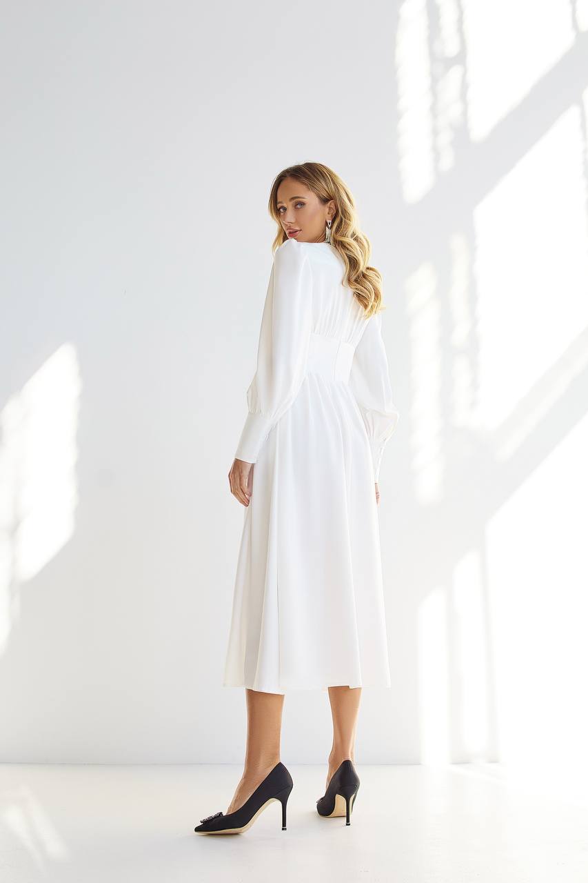 Woman wearing a white dress with long sleeves in a bright room.