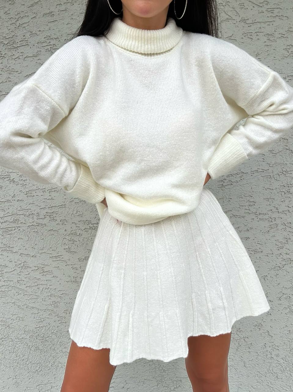Person wearing a white sweater and skirt against a gray background