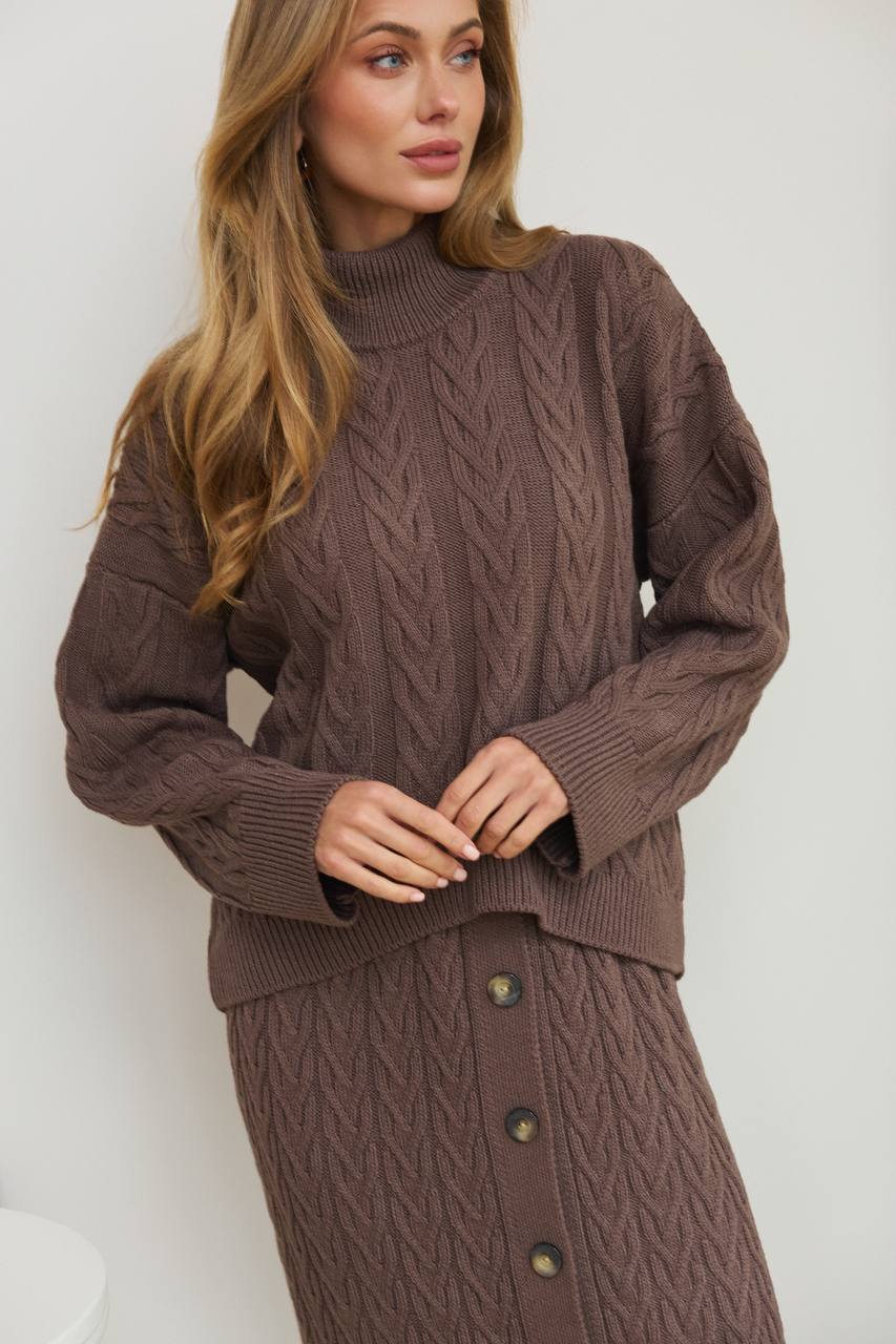 Woman wearing a brown cable knit sweater and skirt set against a white background