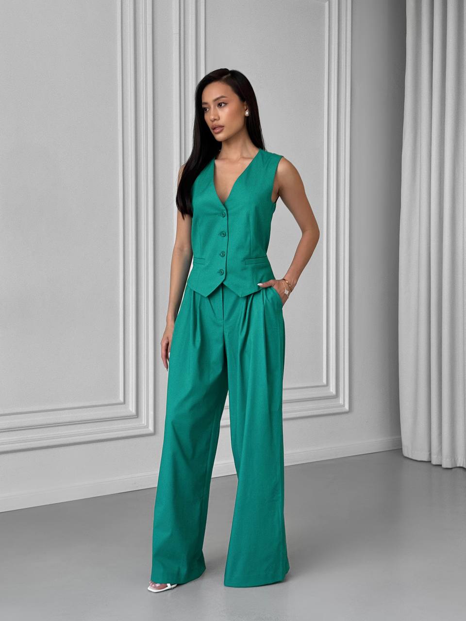 Woman wearing a green jumpsuit standing against a gray wall.