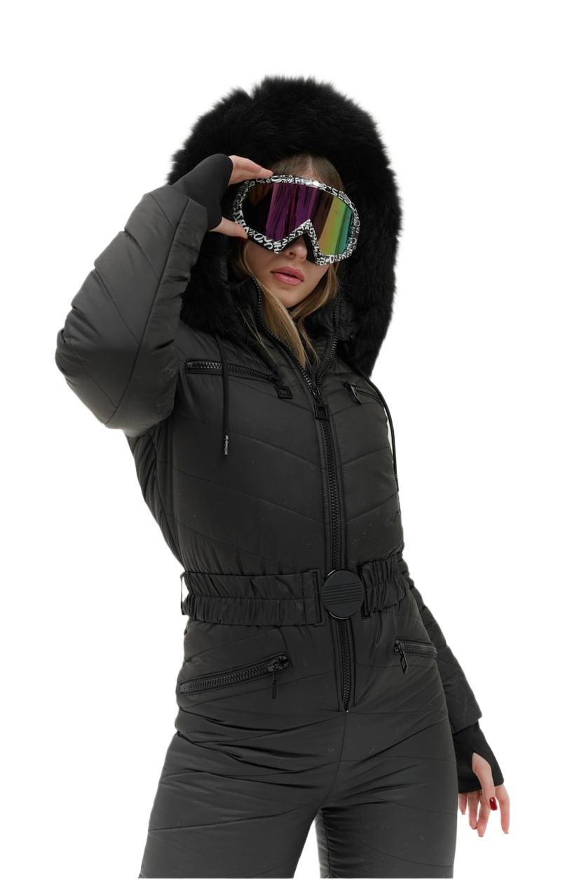 Person wearing a black snowsuit with a fur-lined hood, holding colorful goggles.
