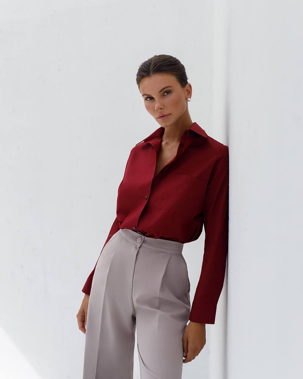 Woman wearing a red blouse and light gray pants against a white background