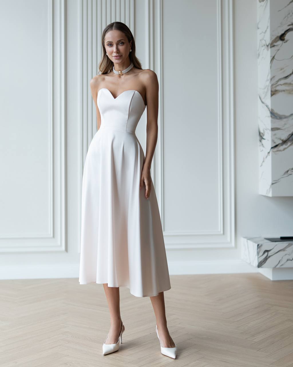 Woman wearing a white strapless dress in an elegant room with marble accents.