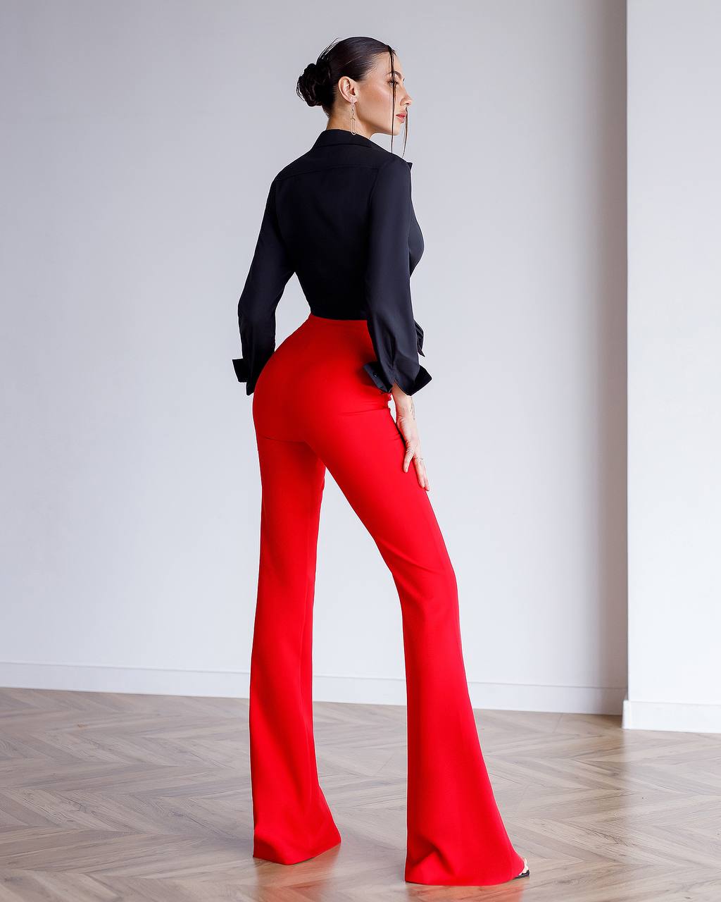 Person wearing a black top and red pants against a white wall.