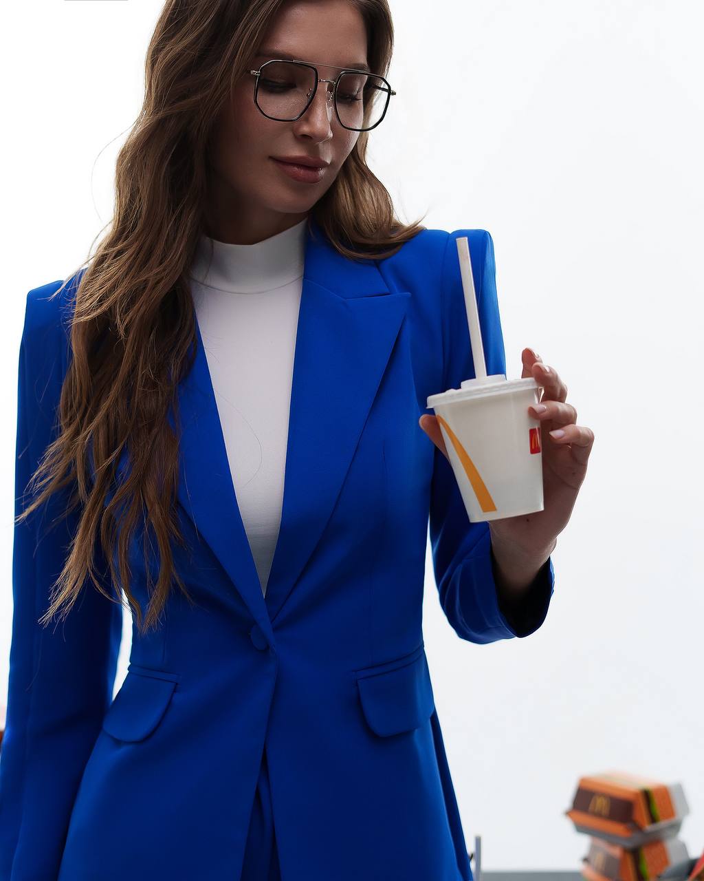 Woman in a blue suit holding a fast food cup with a straw.
