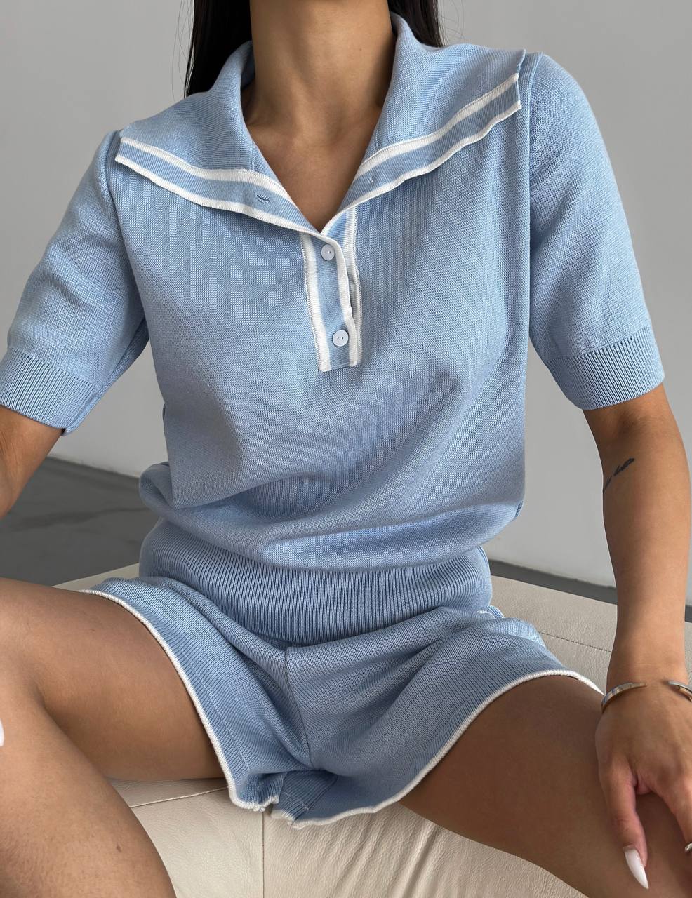 Person wearing a light blue outfit with white trim sitting on a couch.