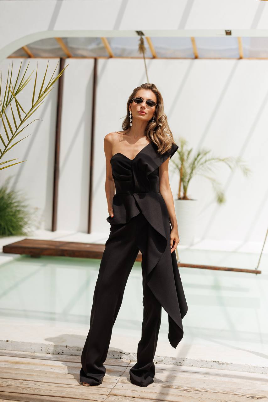 Woman in a black outfit standing in a modern outdoor setting with plants and a pool.