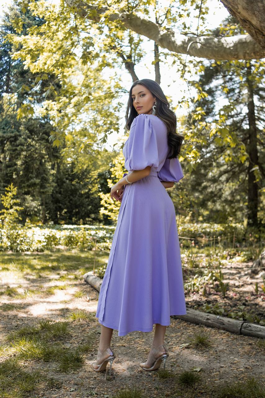 Woman in a purple dress standing in a park with trees and grass in the background