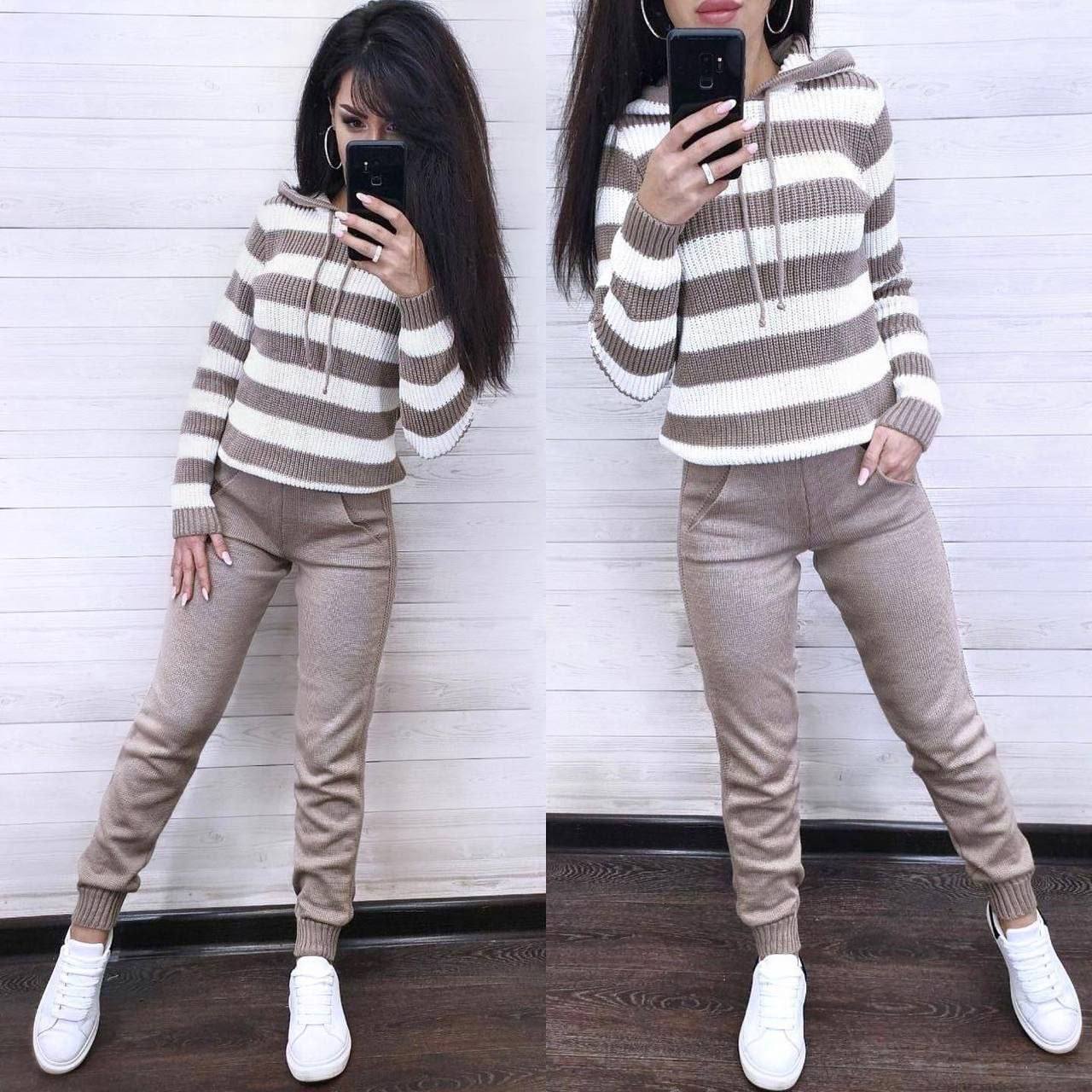 Woman wearing a striped sweater and beige pants, taking a mirror selfie.
