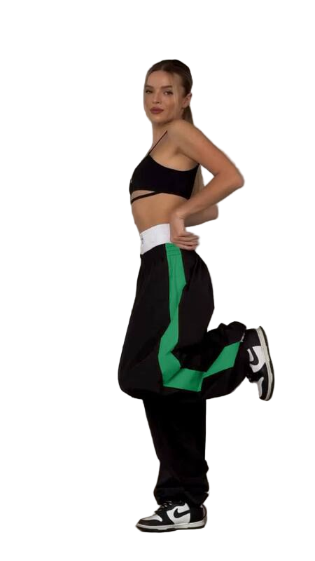 Woman wearing a black sports bra and black pants with green stripes on a white background
