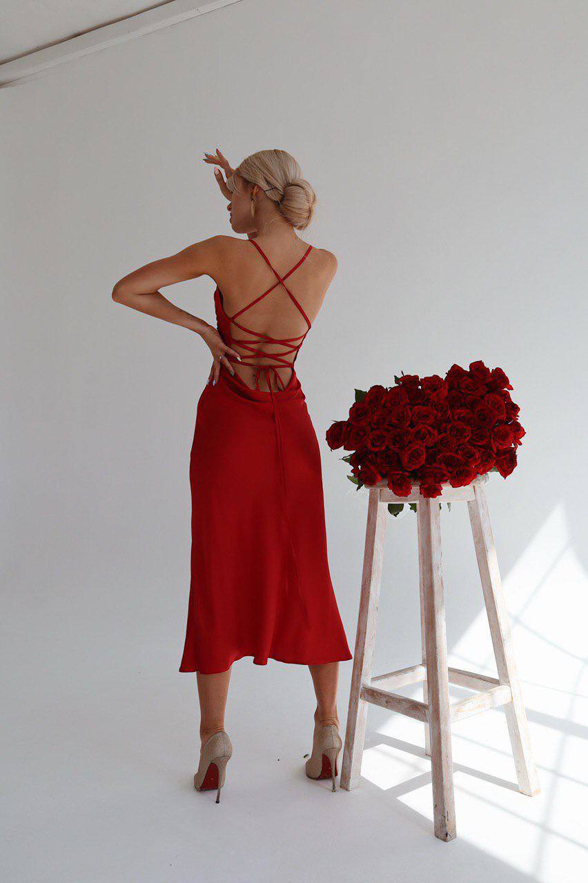 Woman in a red dress standing next to a wooden stool with red roses against a white background