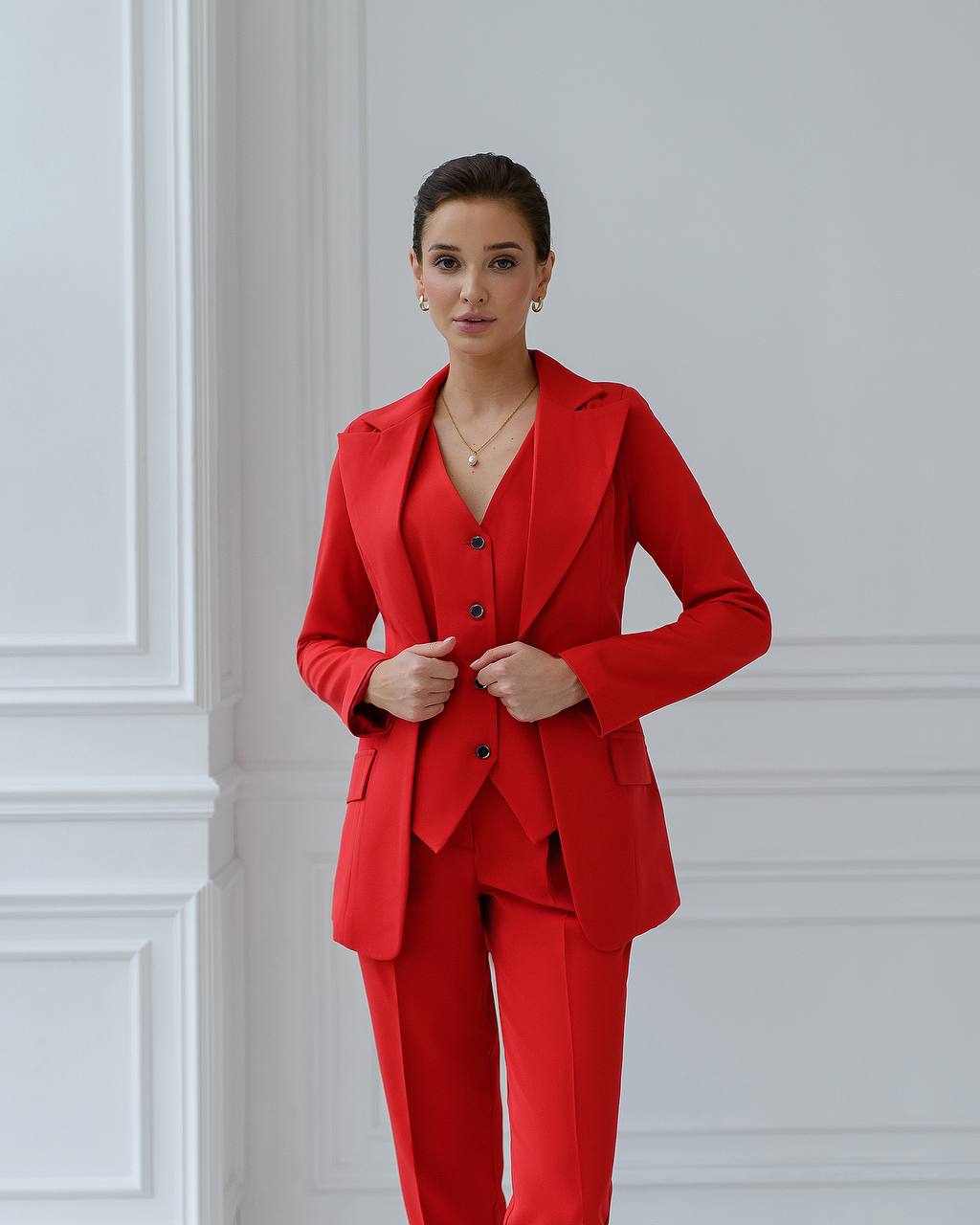 Woman wearing a red suit standing against a white paneled wall.