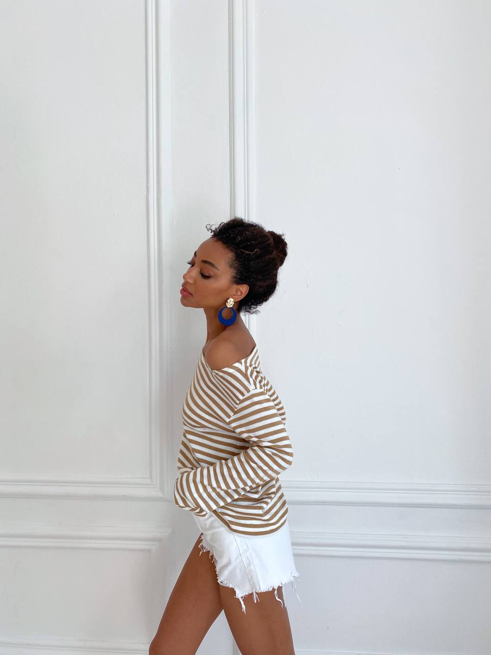 Woman wearing a striped sweater and white shorts against a white wall