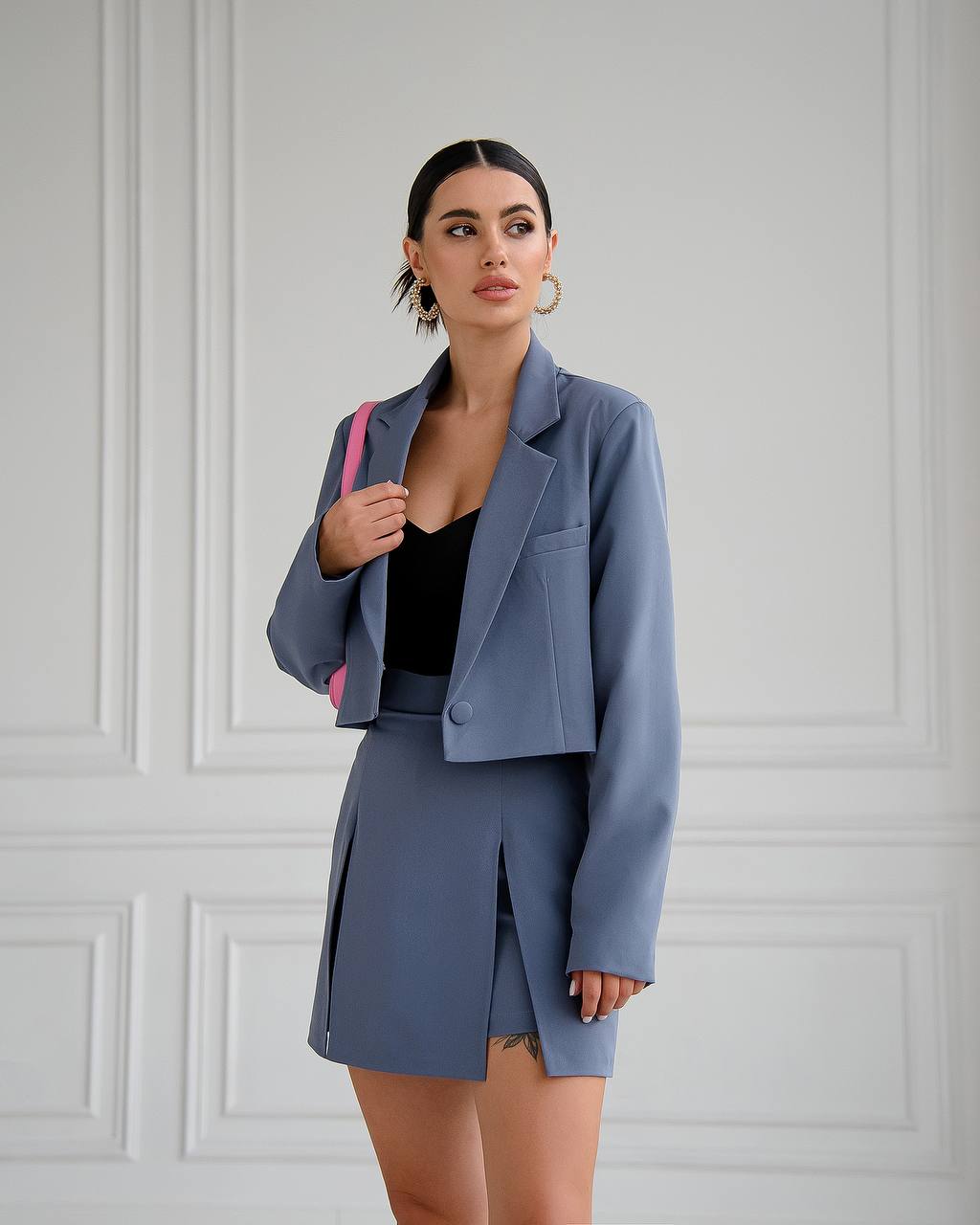 Woman wearing a gray suit with a pink bag against a white wall