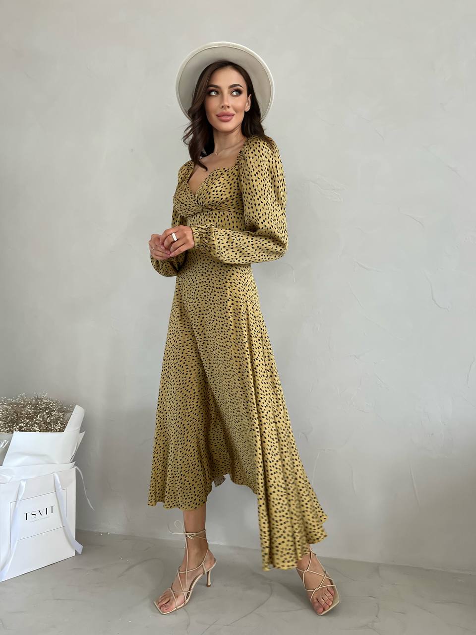 Woman wearing a yellow patterned dress and white hat against a plain background