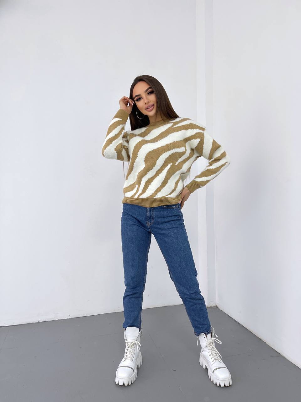 Woman wearing a zebra print sweater, blue jeans, and white sneakers against a white background