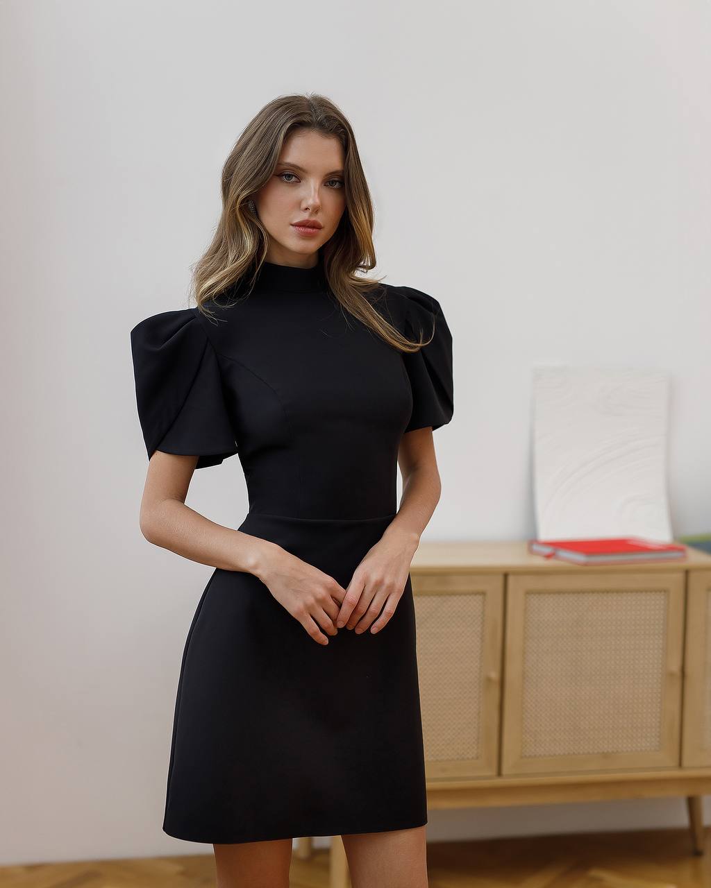 Woman wearing a black dress with puffed sleeves in an indoor setting.