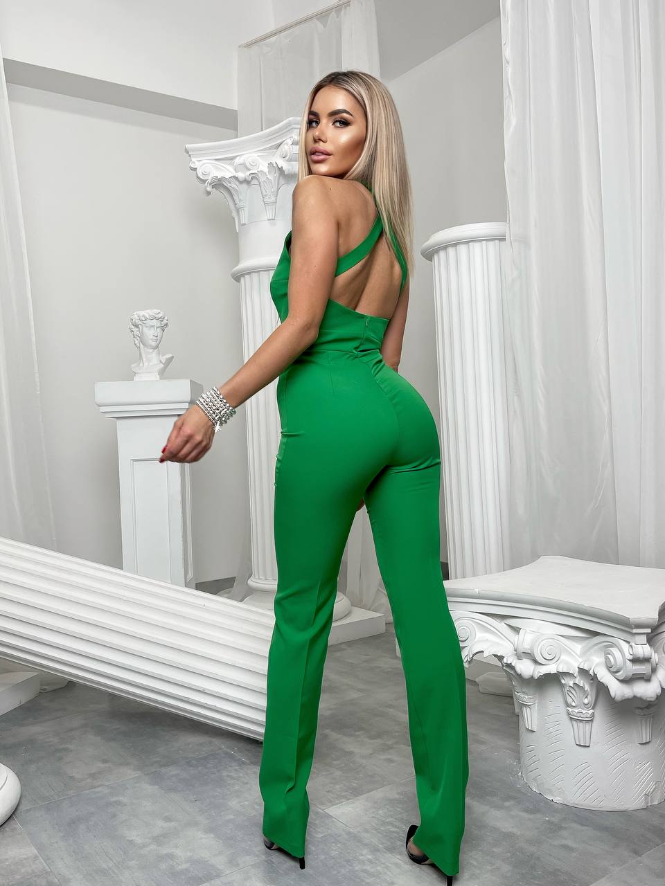 Woman in a green jumpsuit posing in a decorative room with white columns.