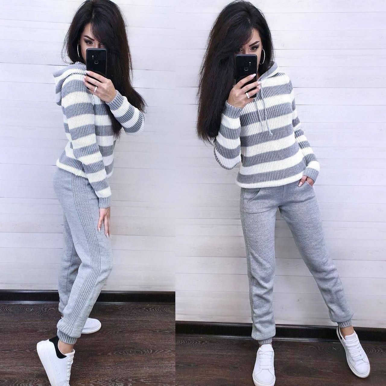 Person wearing a gray and white striped sweater and gray pants, standing against a white wall.