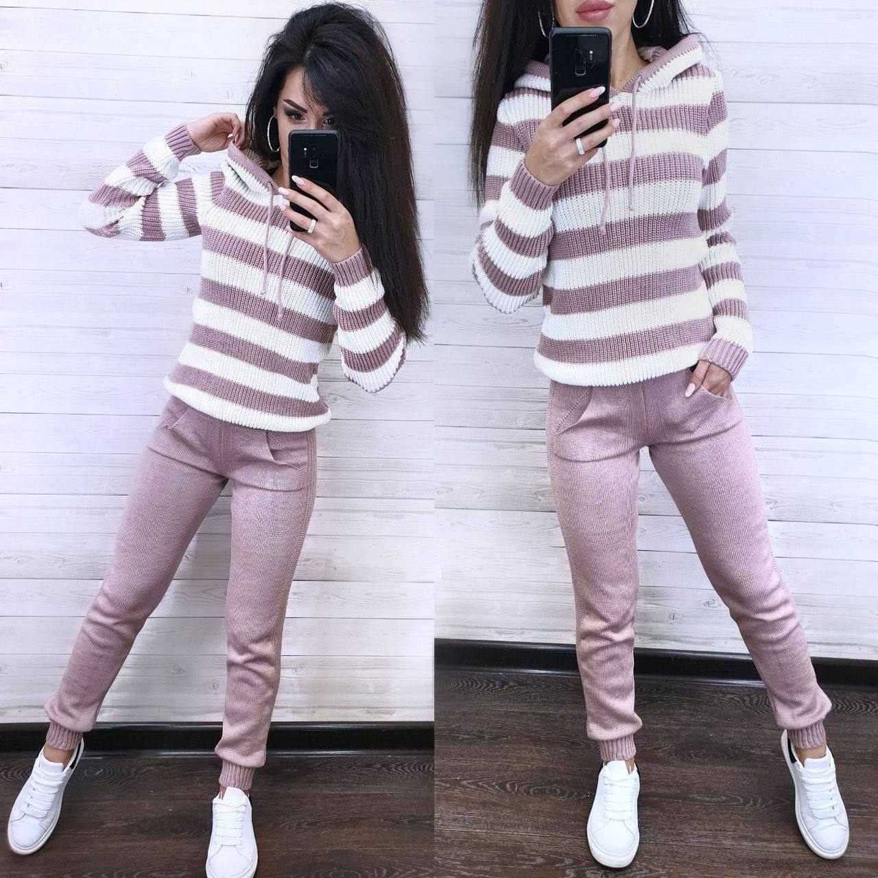 Woman wearing a striped hoodie and pink pants, taking a mirror selfie.