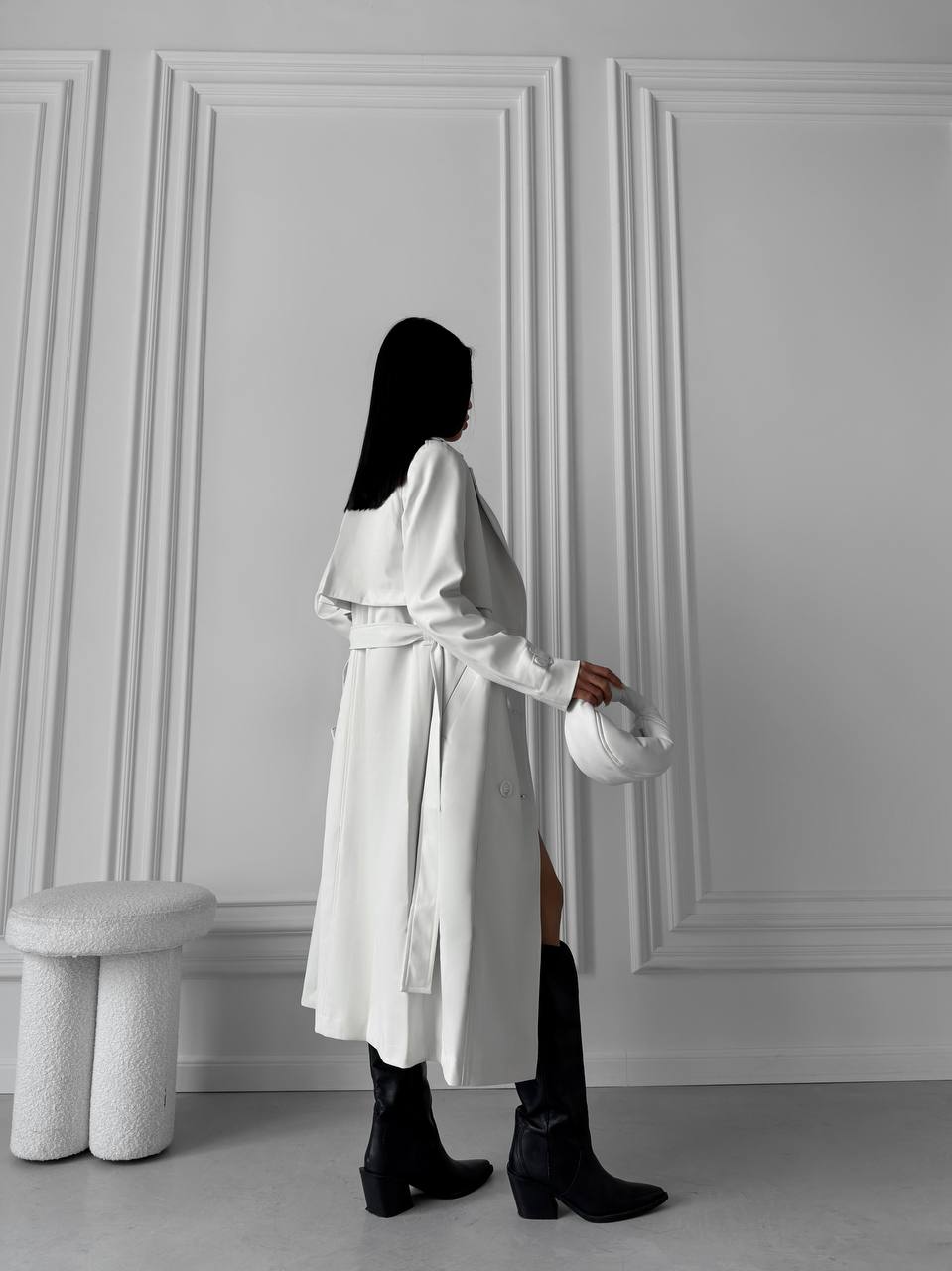 Person wearing a white coat holding a helmet against a gray paneled wall.